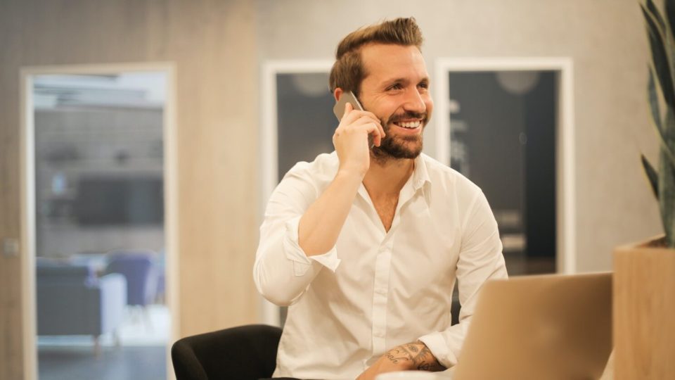 Businessman sitting at a bar happily talking on his mobile phone while working