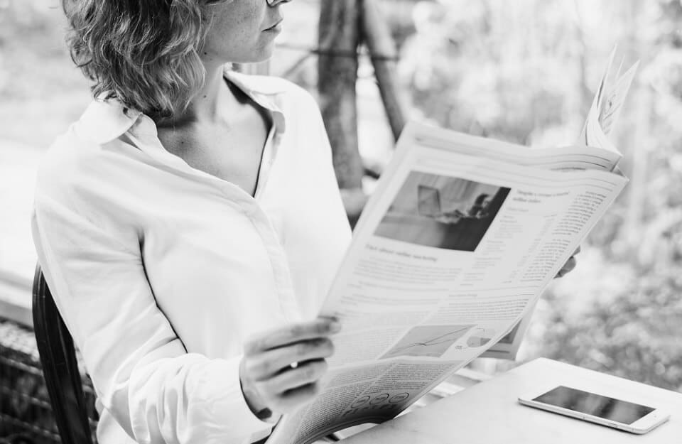 A woman dressed in white reading a traditional newspaper