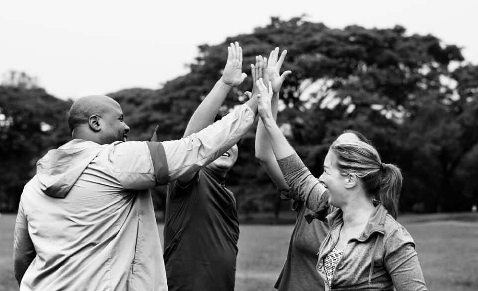 Group of people coming together to high five in a park - understanding equality