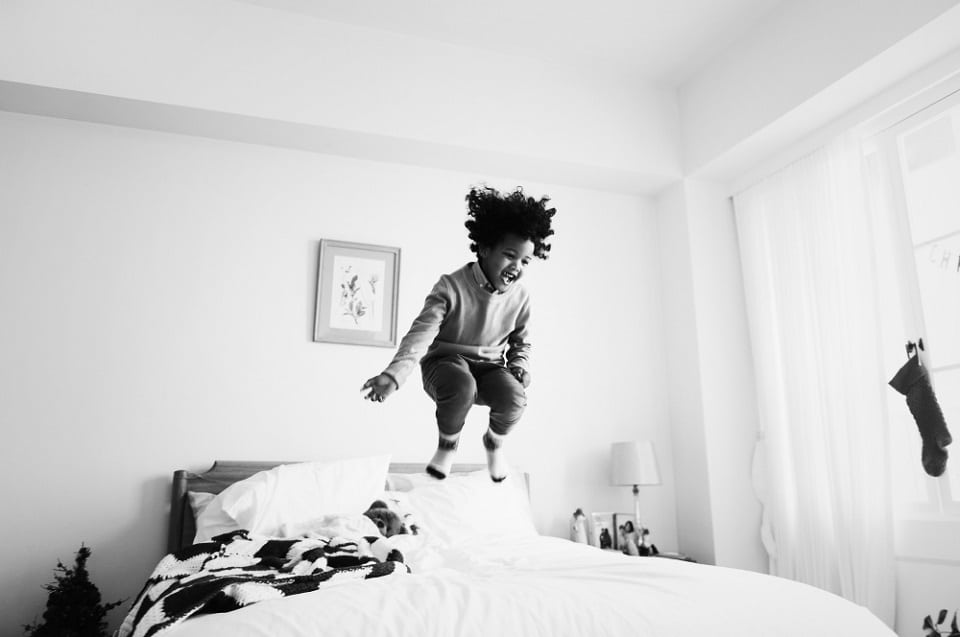 A young kid showing happiness and excitement by jumping excitedly on the bed