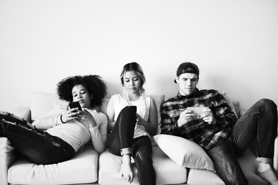 Three gen z friends sitting on a couch watching youtube videos on their mobile phones