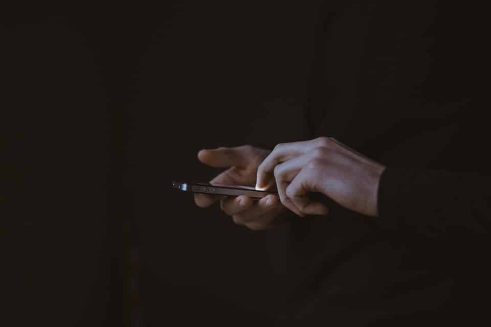 A man scrolling through social media on his phone against a black background